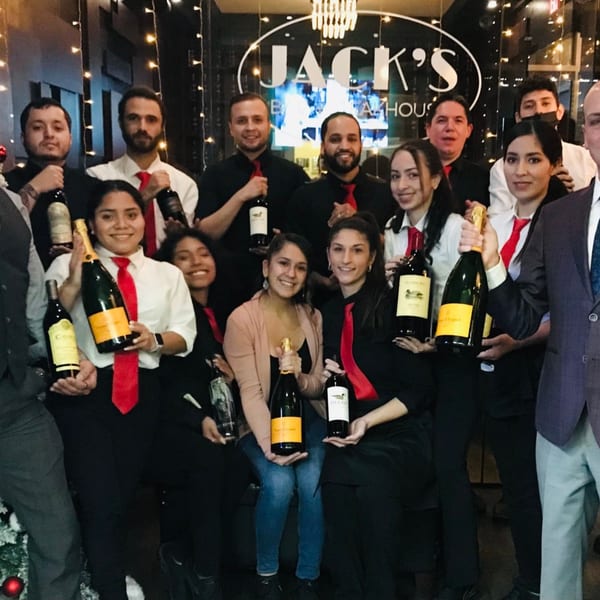 Jack's Bar And Steakhouse staff, dressed in black and white with red ties, holding wine bottles.