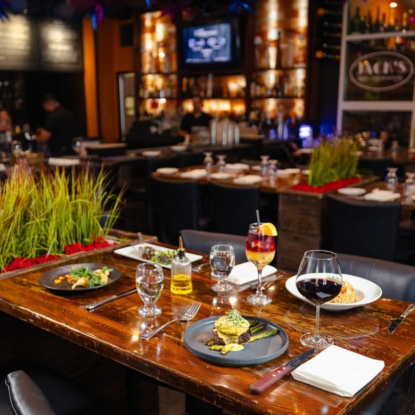 A Jack's Bar And Steakhouse table set with steak, drinks, and appetizers in a dimly lit dining room.
