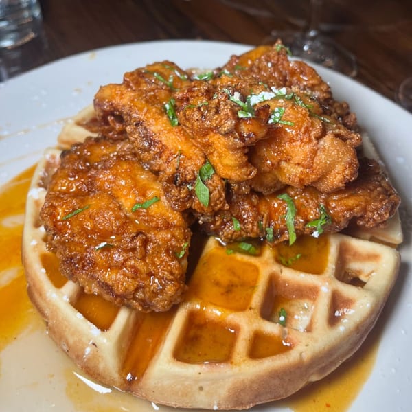Crispy fried chicken pieces drizzled with syrup and herbs, served atop a golden waffle.
