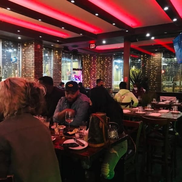 Diners seated at tables in a dimly lit steakhouse with red ceiling lights and brick walls.