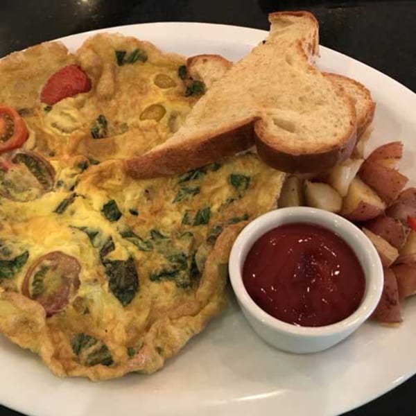 A breakfast plate with a large omelet, toast, home fries, and a side of ketchup.