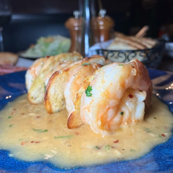 Shrimp scampi with toasted bread slices in a creamy sauce on a blue plate at Jack's Bar And Steakhouse.