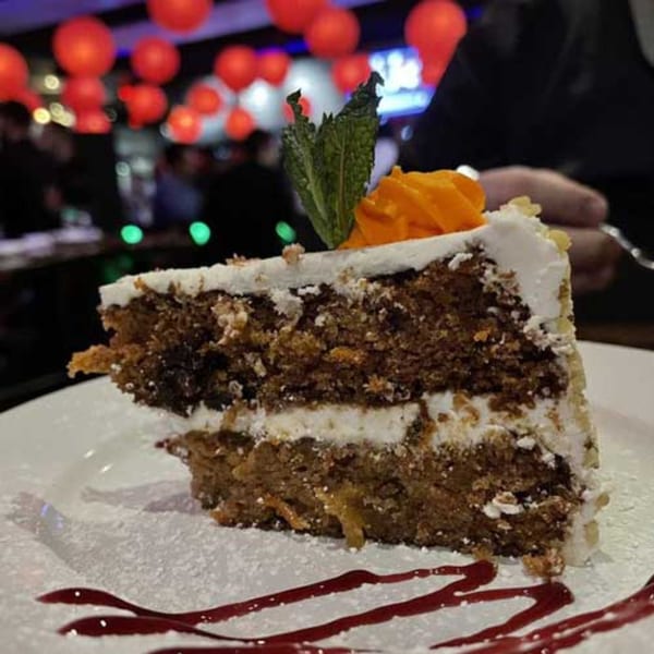 A slice of carrot cake with cream cheese frosting, garnished with mint and orange peel, on a white plate.