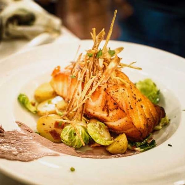 Grilled salmon fillet with crispy fried onions, roasted potatoes, and Brussels sprouts on a white plate.