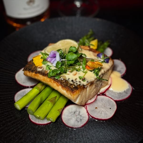 Pan-seared fish with sauce, microgreens, edible flowers, lime, asparagus, and radish slices.
