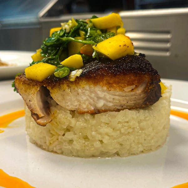 Seared fish with mango salsa and greens, served atop a cylinder of creamy risotto.